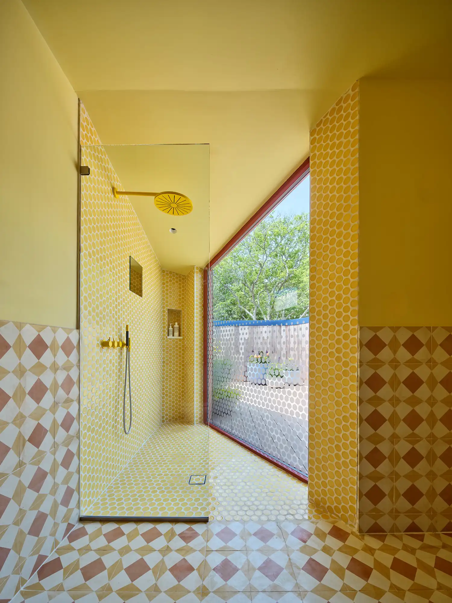 A bathroom with yellow mosaic tiles and a large window overlooking the woods.