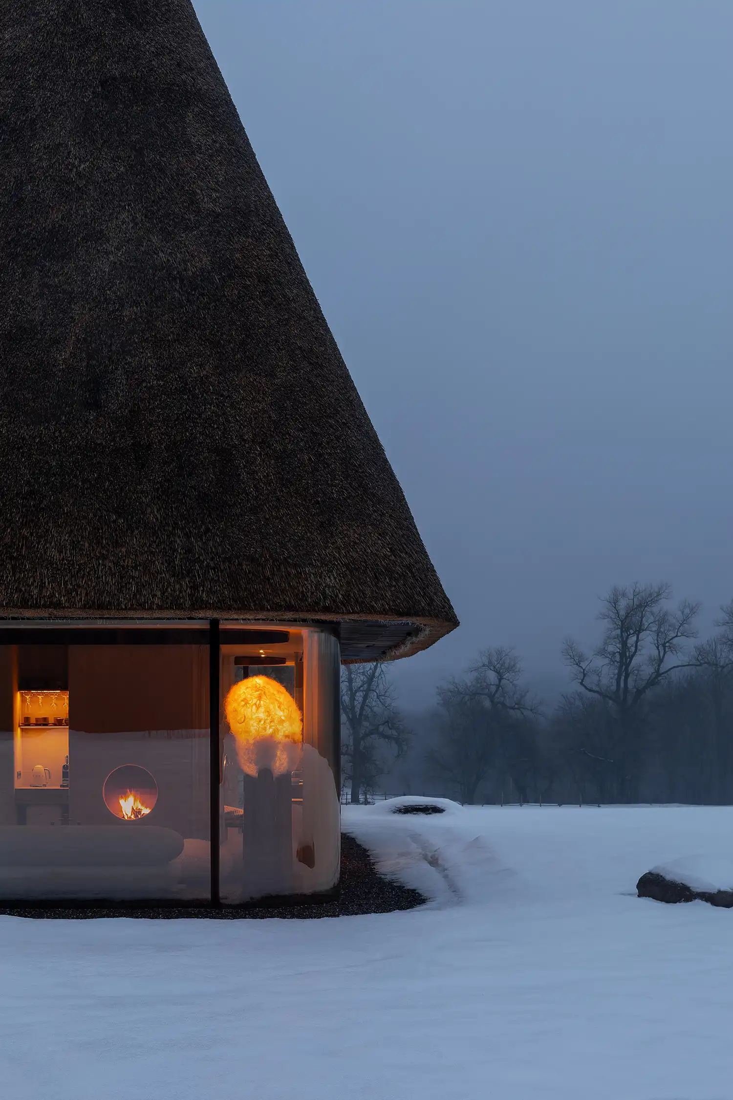 Twilight view of a lit guesthouse with a glowing fireplace and sculptural lamp.