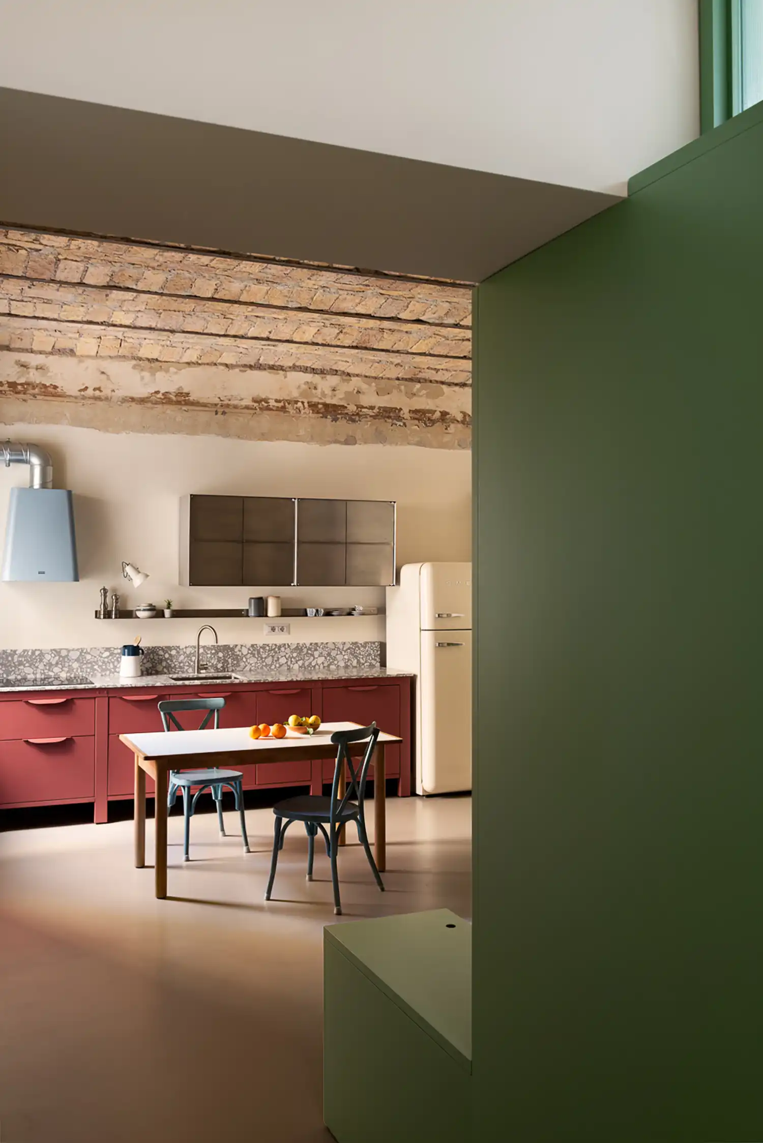 View from behind a green architectural element looking into the red and cream kitchen.