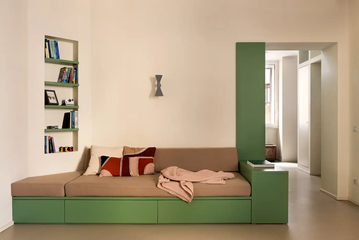 Built-in beige sofa integrated into a green wooden base with recessed shelving.