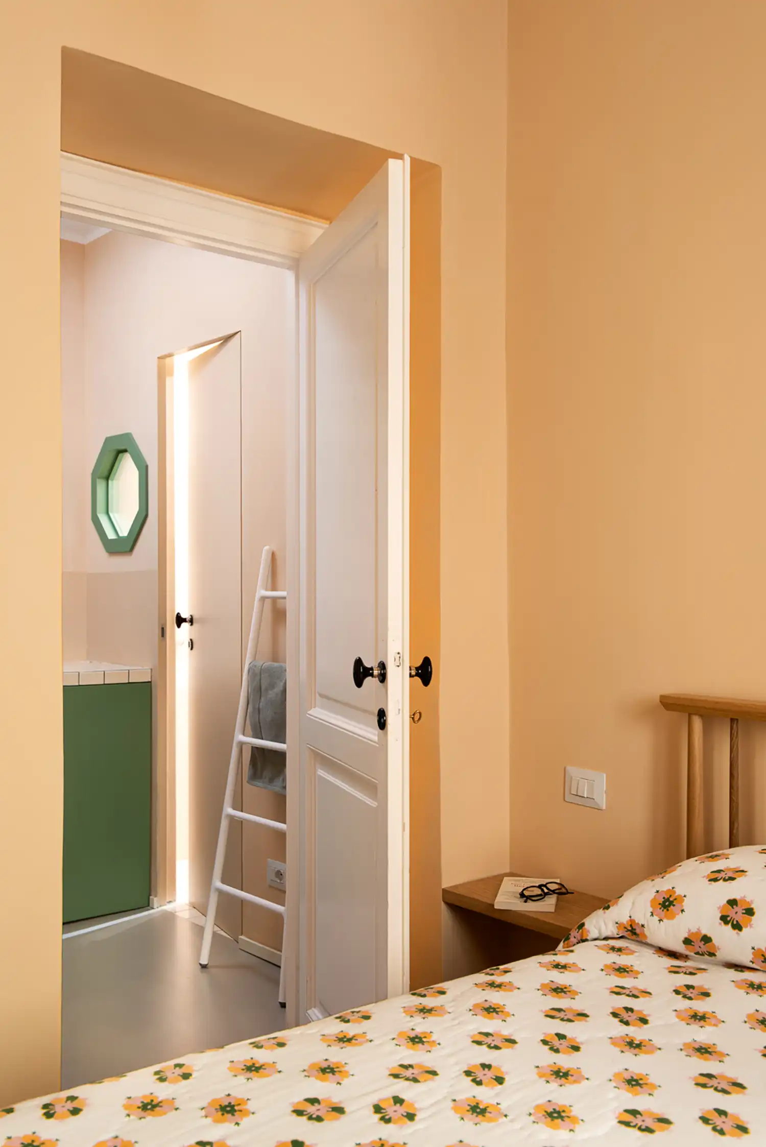 Peaches-and-cream bedroom view looking through a white door toward a green bathroom vanity.