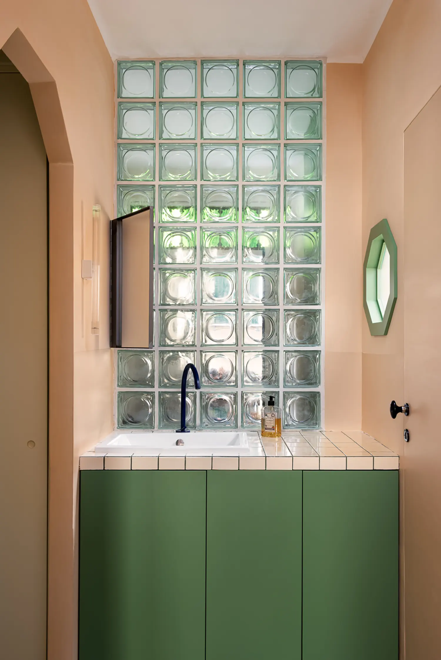 Compact bathroom vanity with a green cabinet, tiled countertop, and large glass block partition.