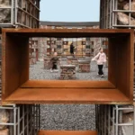 A framed view through a rusted metal void showing children playing in the Echo Plaza.
