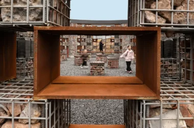A framed view through a rusted metal void showing children playing in the Echo Plaza.