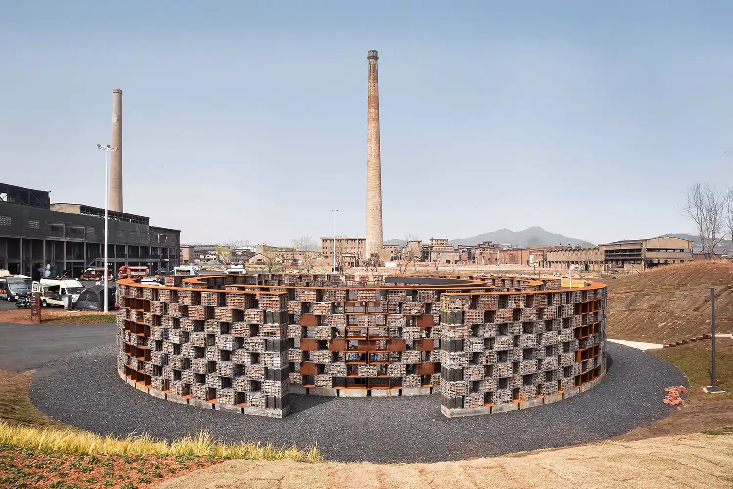 Wide shot of the circular Echo of the Ruins Sound Museum with industrial chimneys in the background.