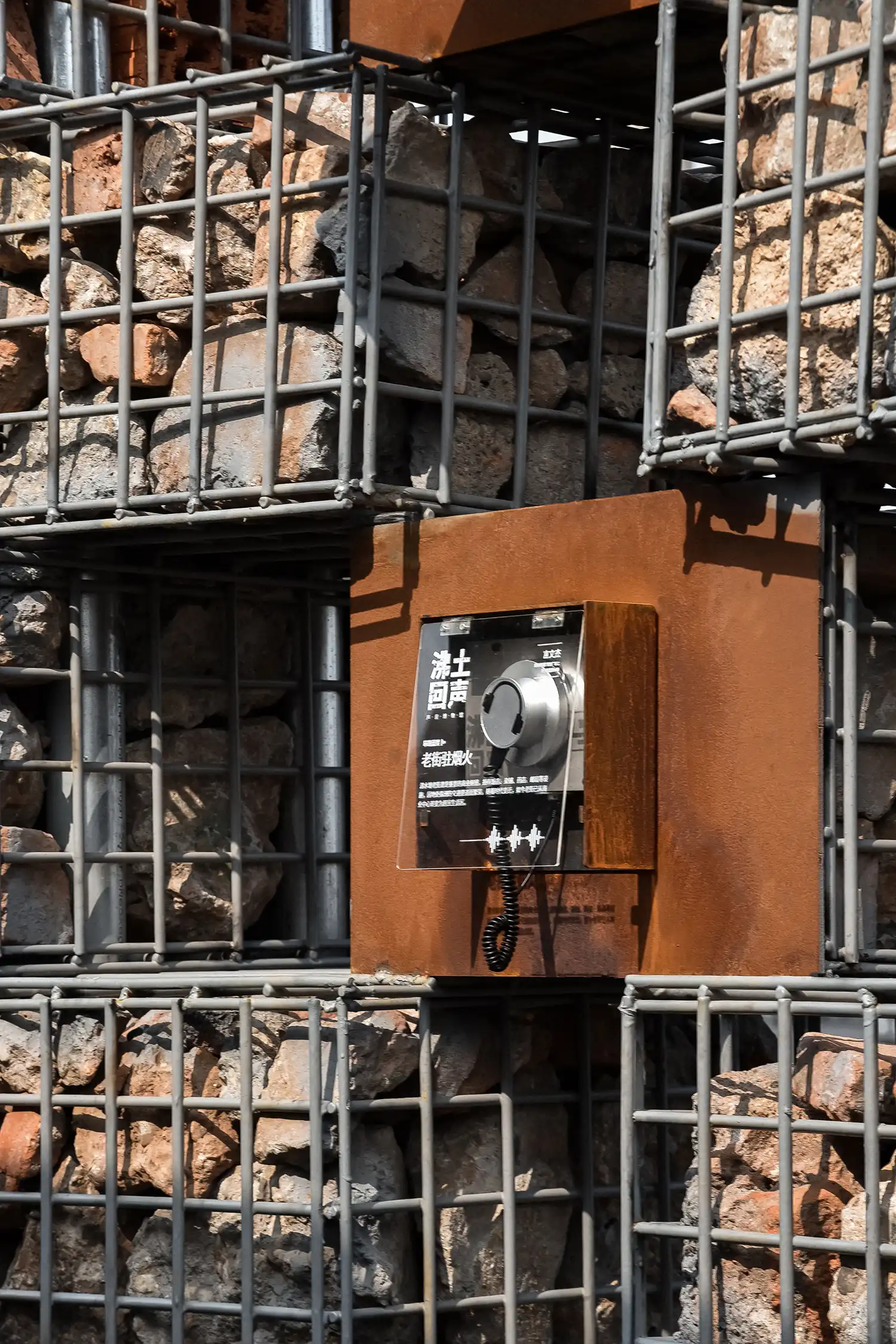 Close-up of a magnetic headphone station mounted on a rusted metal plate within a stone wall.