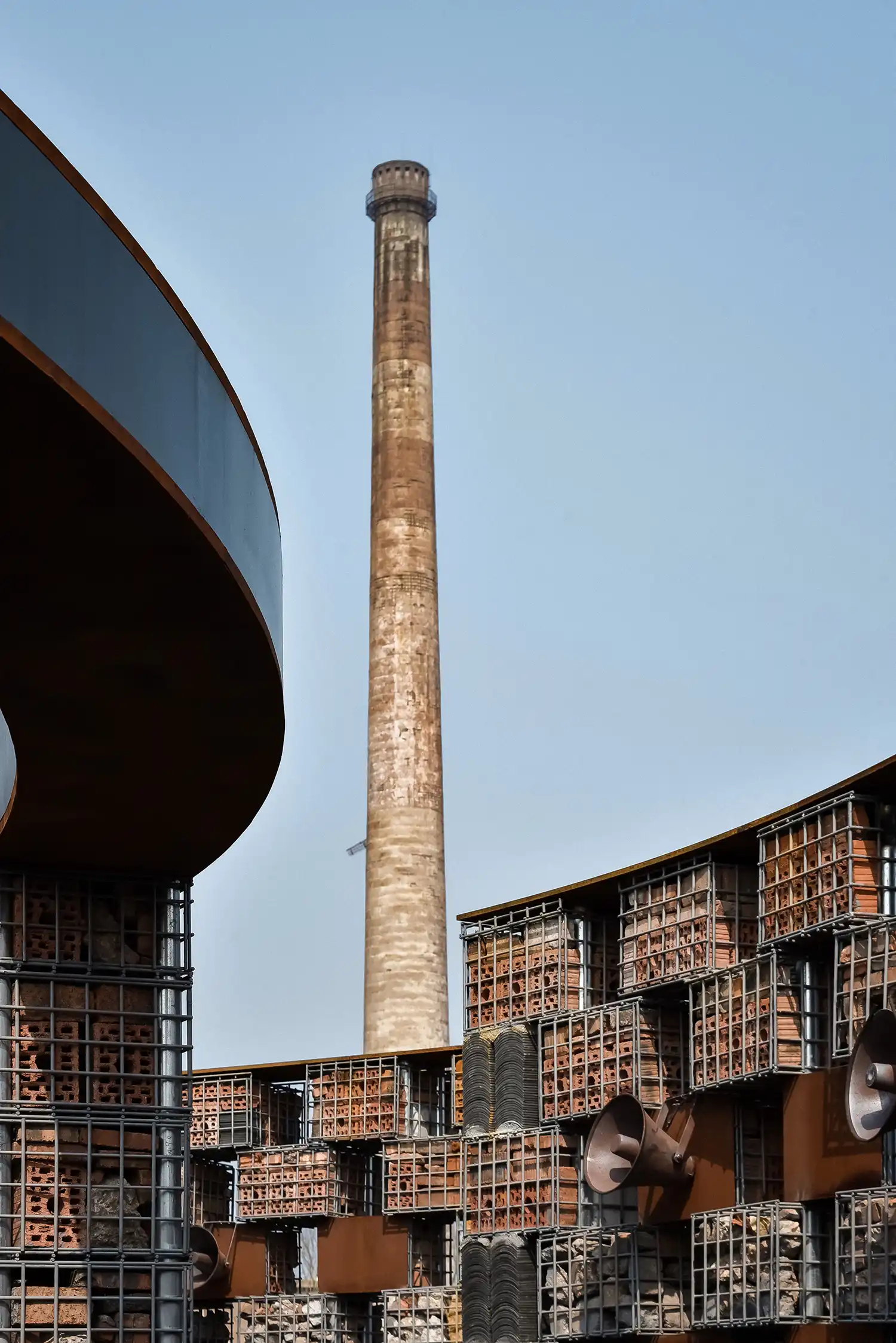 Low-angle view looking up at a tall brick chimney framed by the museum’s curved walls and speakers.
