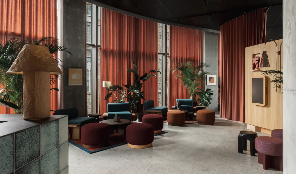 Lounge area at Locke Copenhagen featuring rust-toned curtains, teal armchairs, and terracotta poufs against concrete columns.