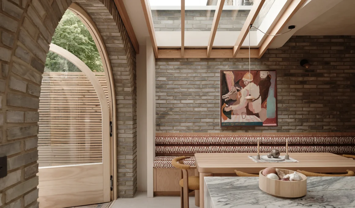 Internal view of a dining area with a brick wall, timber-framed skylight, and a large arched glass door leading to a patio.