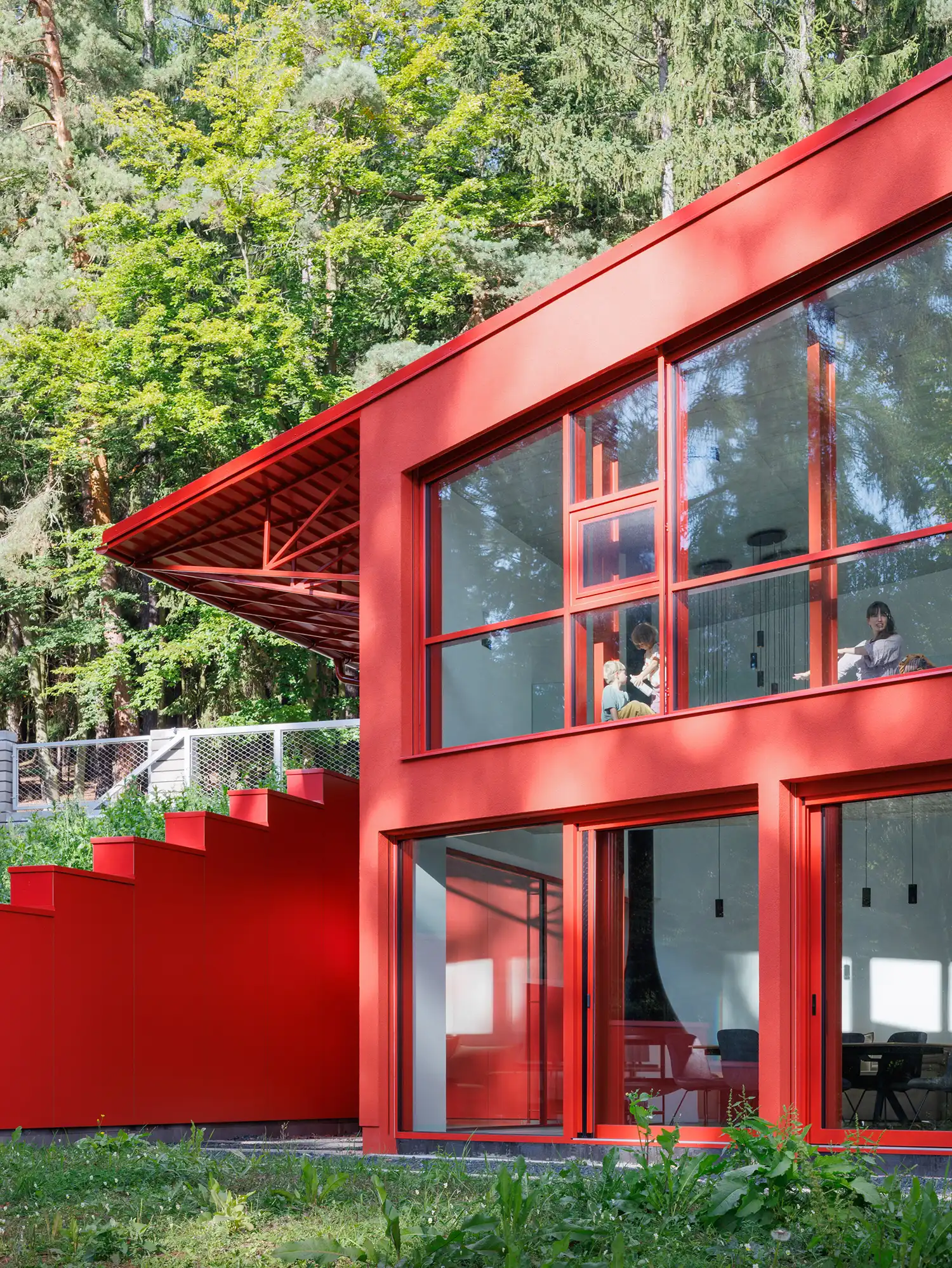 Close-up of the red exterior facade with large glass windows and an external red staircase against forest greenery.