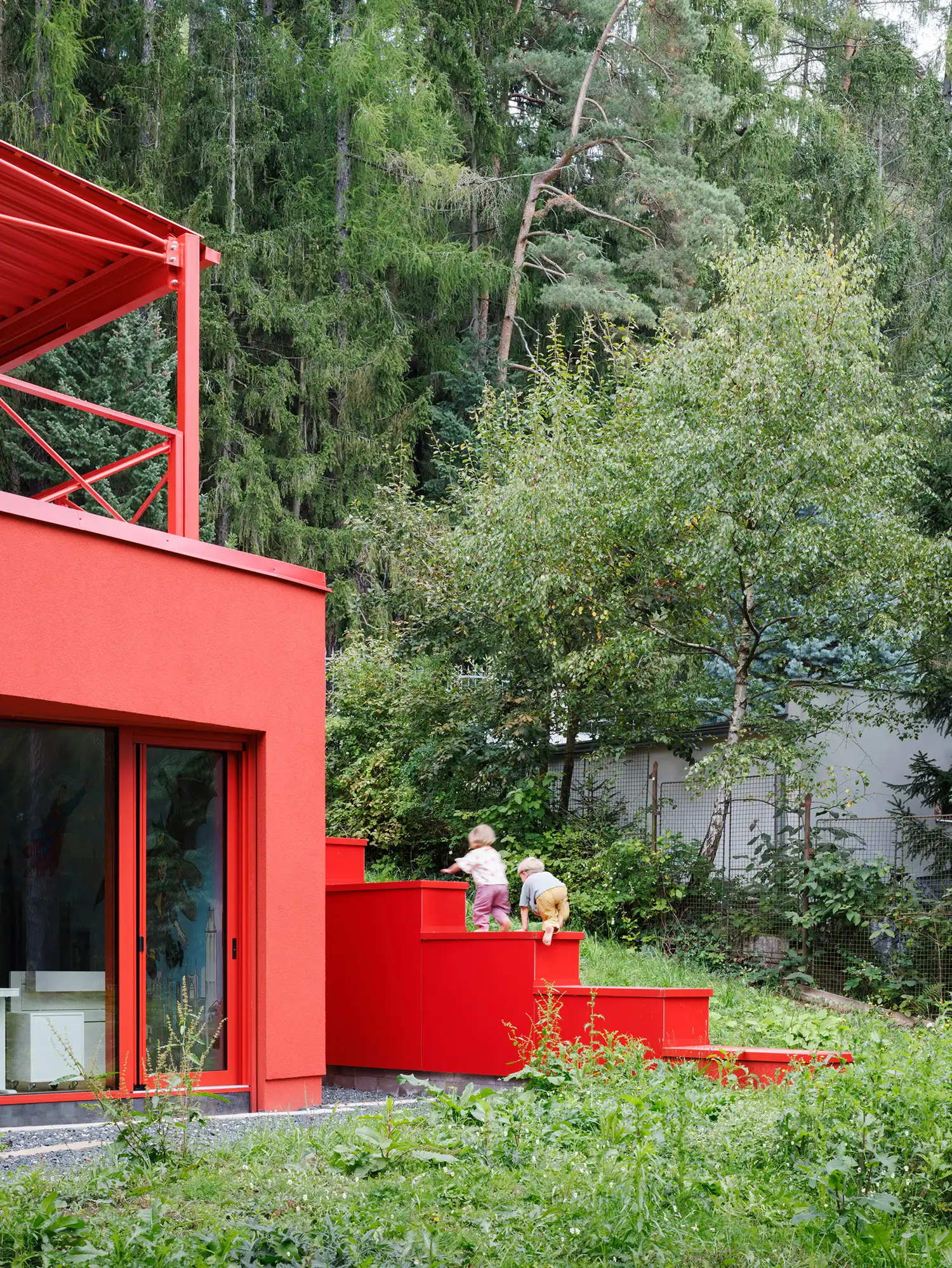 Children climbing a sculptural red exterior staircase built into the side of the red villa.