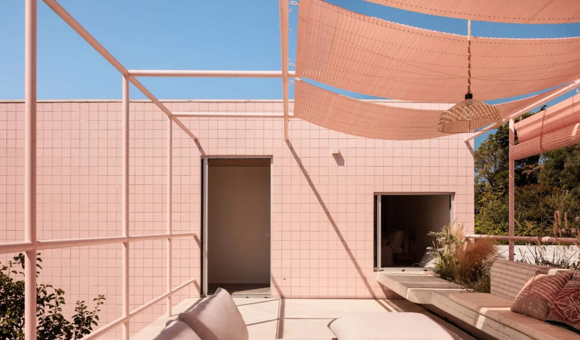 An elevated view of the rooftop terrace at Casa em Galamares by atelier RUA, featuring a pink tiled facade, slatted shade sails, and integrated concrete seating.