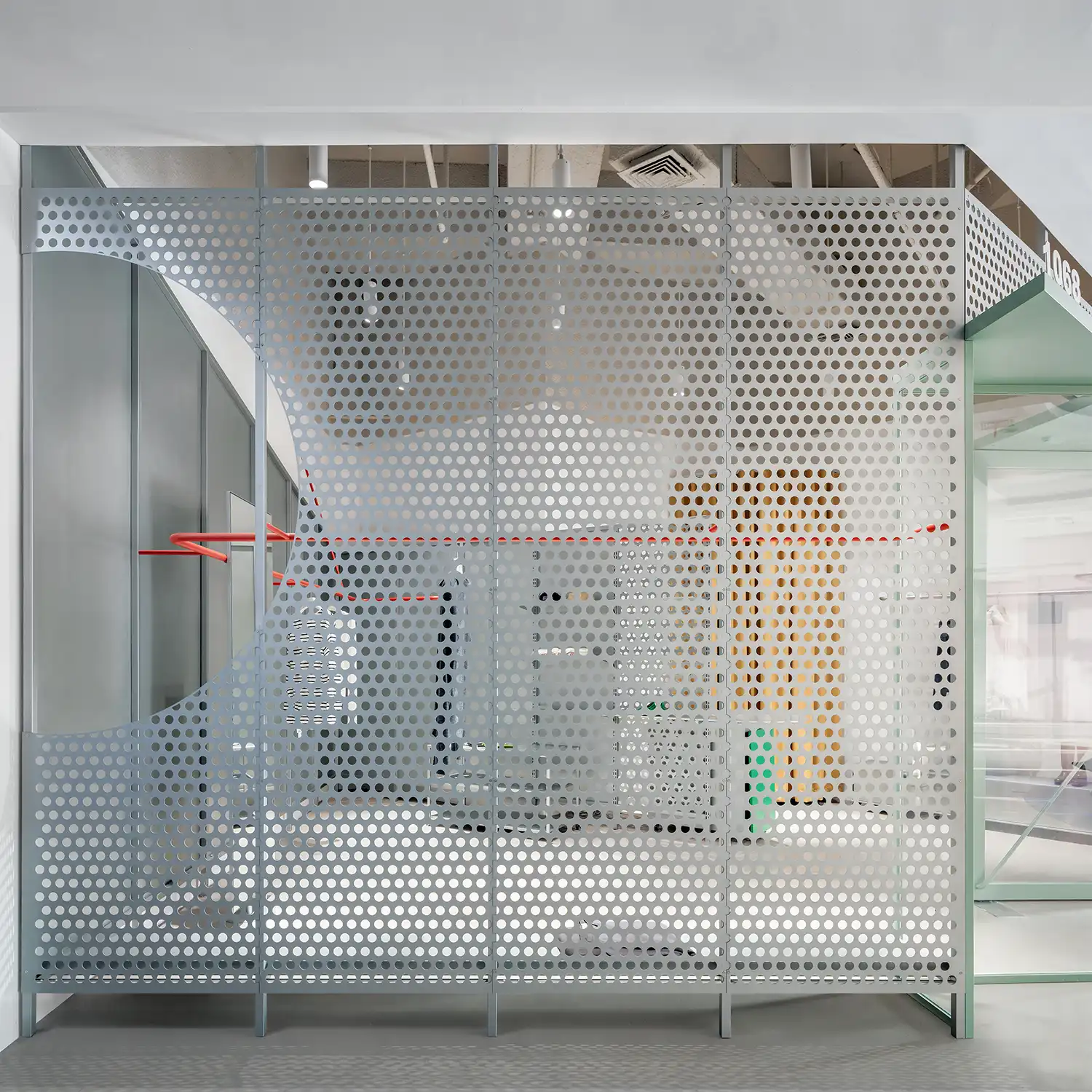 Close-up of grey perforated metal partition with a circular cutout revealing the retail interior.