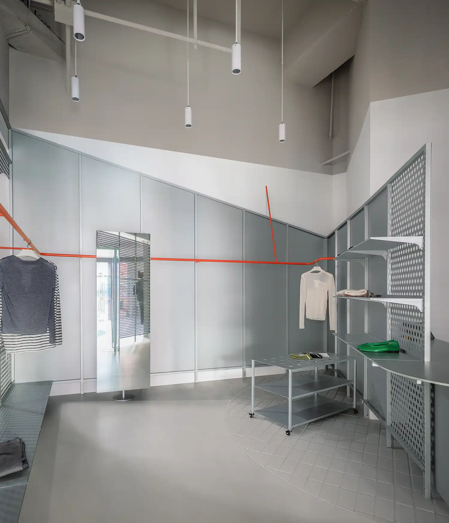 Minimalist retail interior with a continuous orange clothing rail wrapping around grey industrial panels.