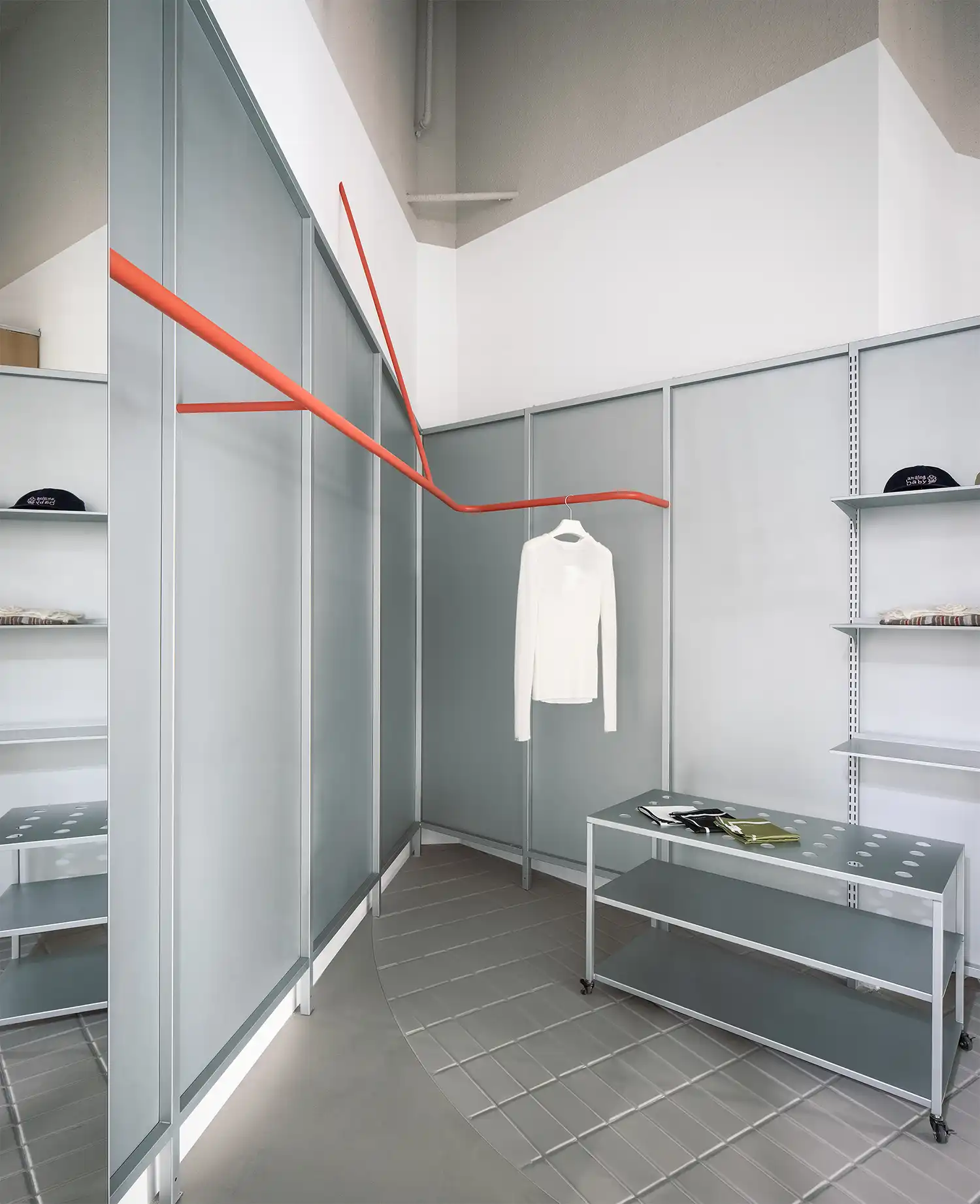 Detailed view of the orange clothing rail intersecting with modular grey panels and minimalist shelving.