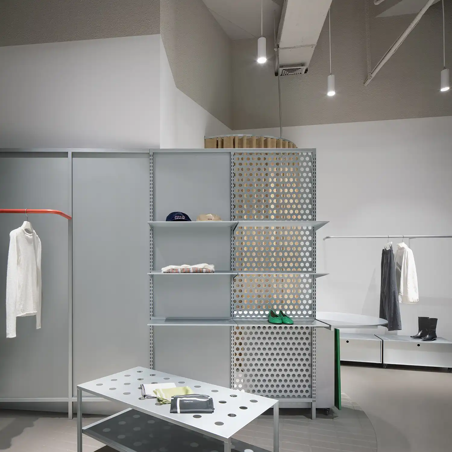 Interior display area with perforated metal screens, minimalist pendants, and a grey display table.