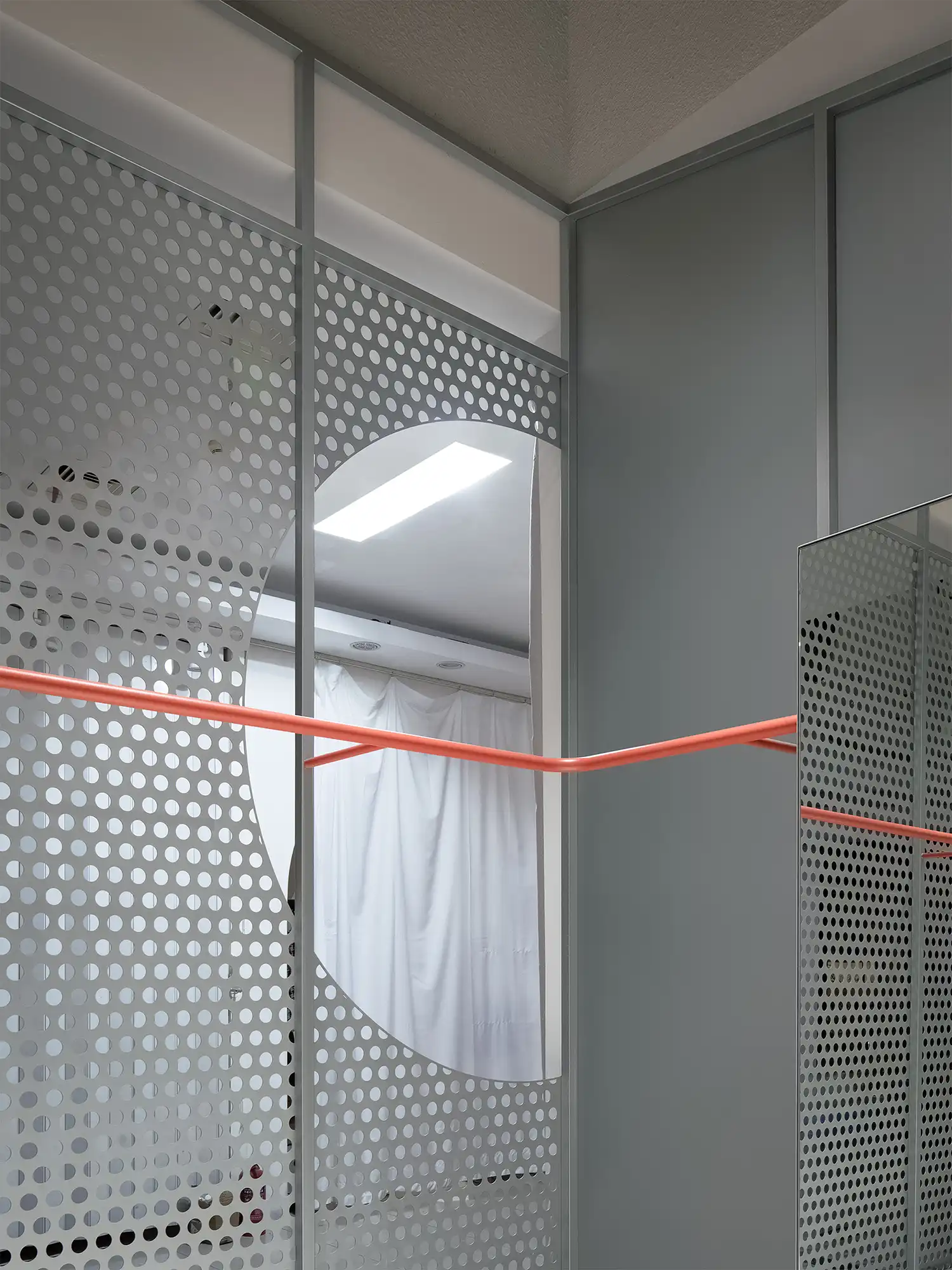 Close-up of the interaction between the orange metal rail, a mirror, and the perforated screen.