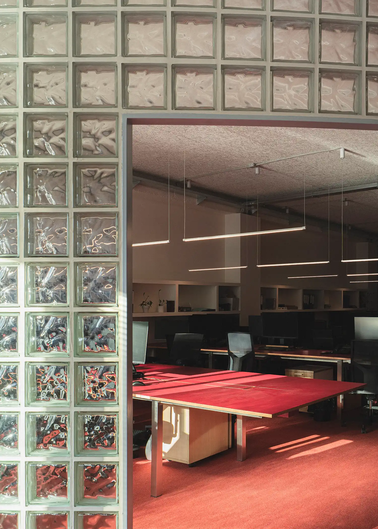 Large communal red worktable positioned behind a translucent glass-block partition.