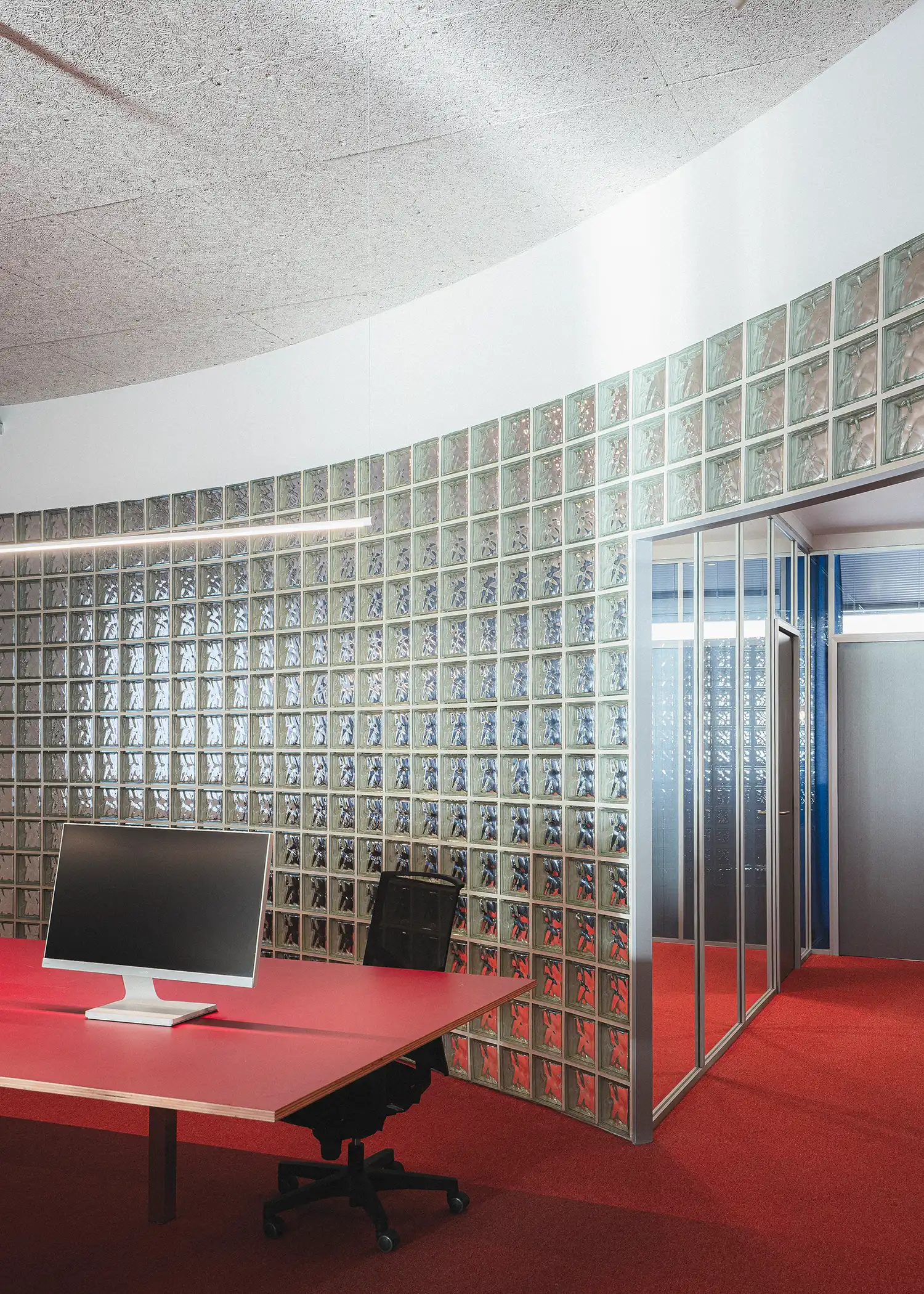 A wide-spanning curved glass-block wall reflecting red floor tones in a bright office.