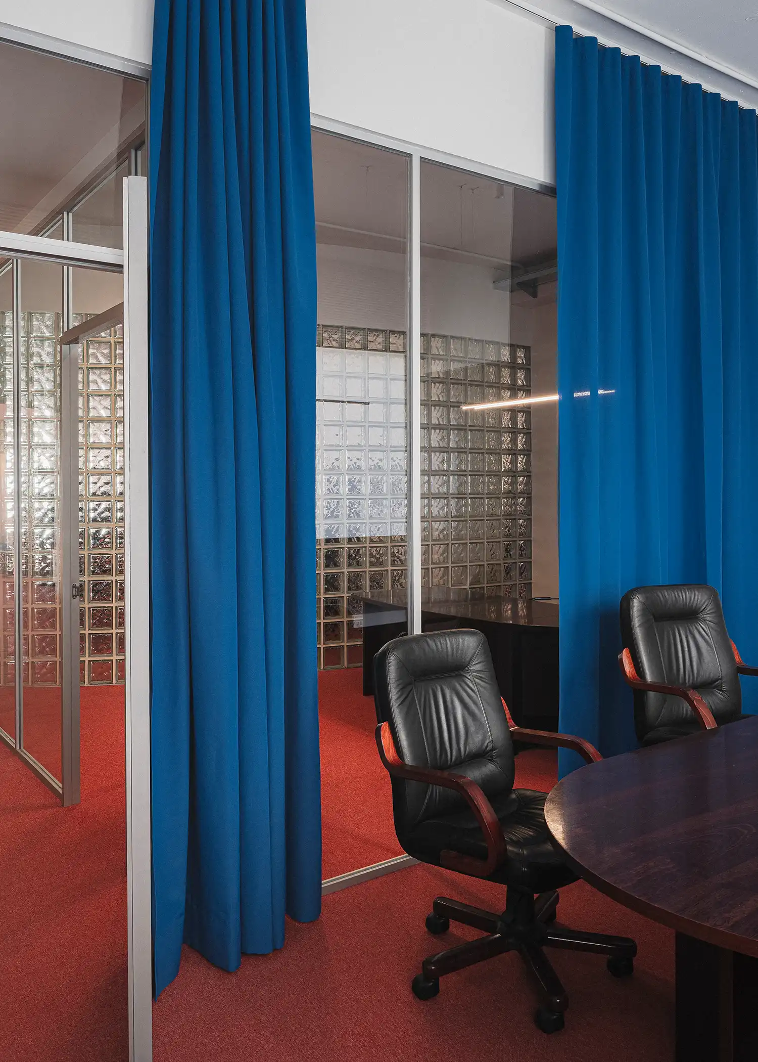 Deep blue curtains and black leather chairs in a glass-walled meeting room with red carpet.