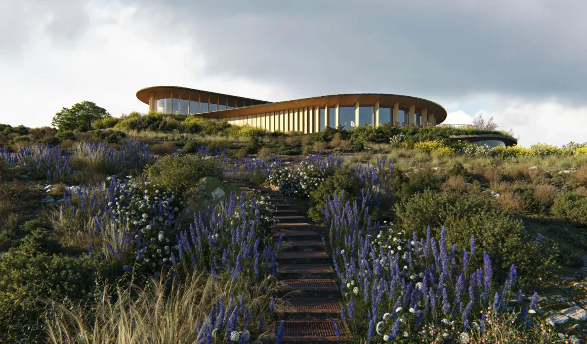 A low-angle view of a curved timber and glass building on a grassy hill, accessed by a weathered metal staircase. Purple and white flowers flank the path under a cloudy sky.