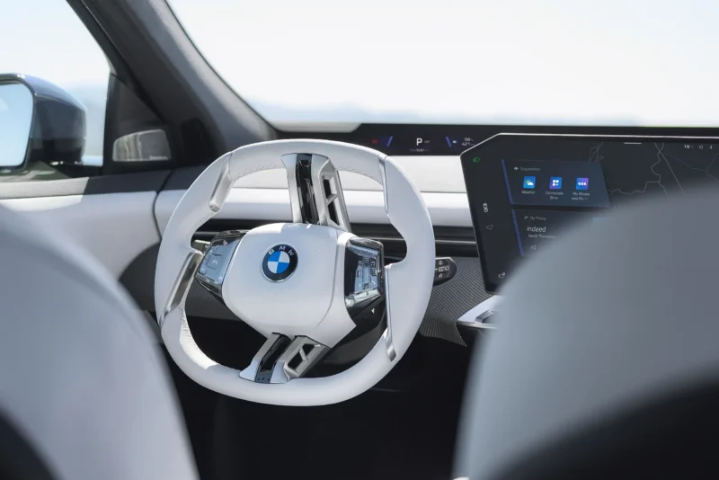 Close-up of 2026 BMW iX3 white steering wheel and central touchscreen interface.