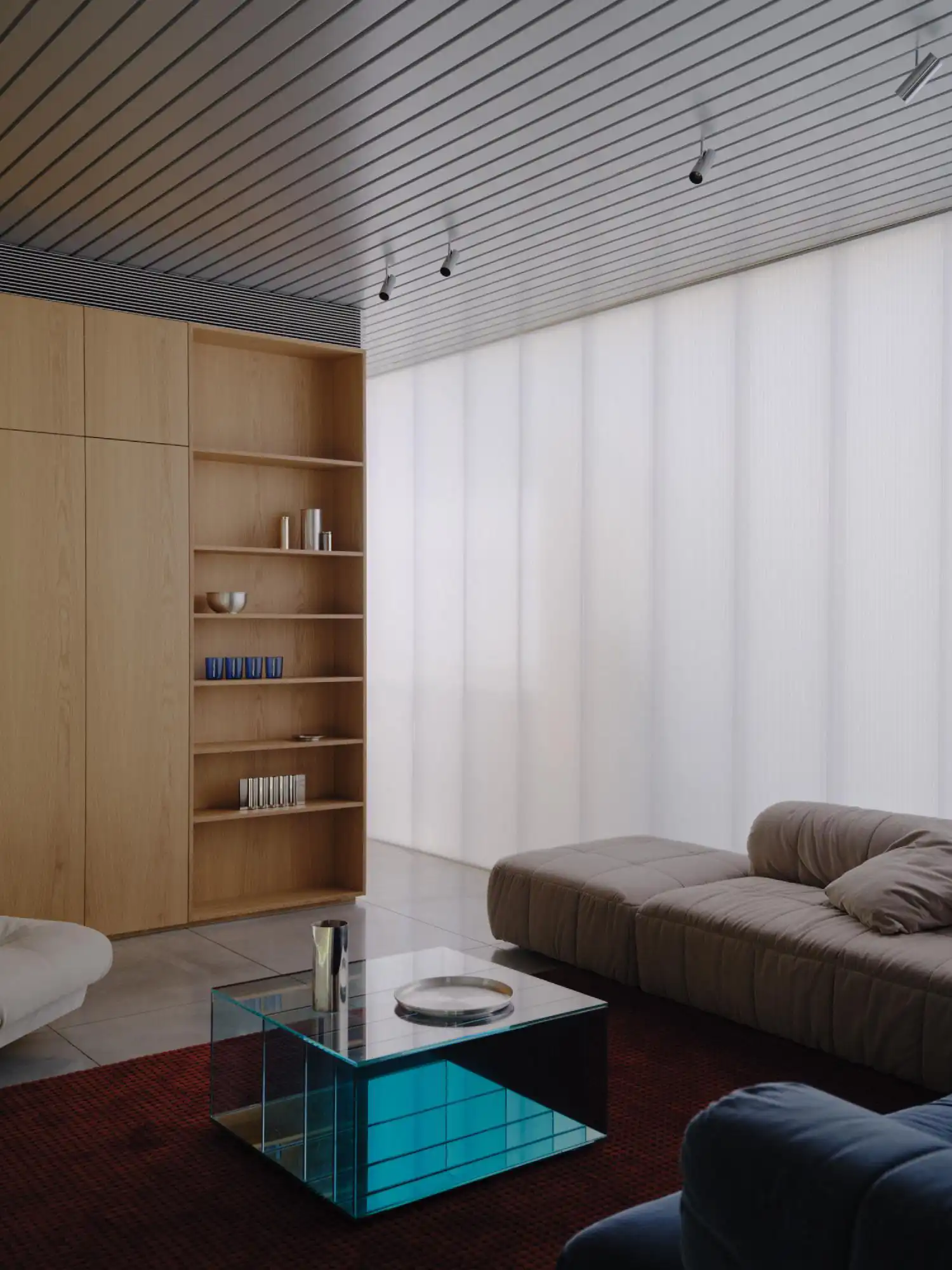 Modern living room with a modular tan sofa, a glass coffee table, and oak shelving against a glowing wall.