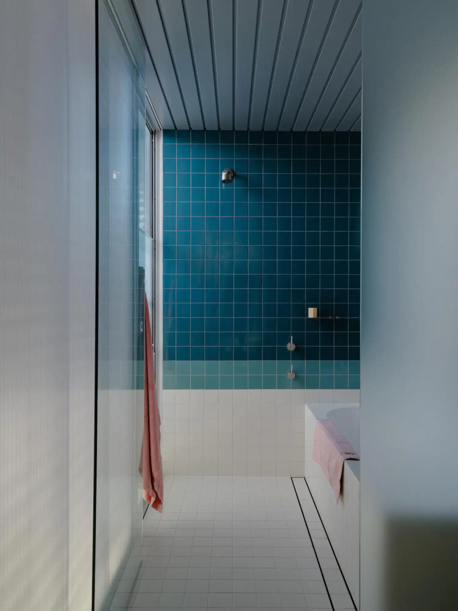 Contemporary bathroom with deep teal, light green, and white square tiles and a glass shower partition.
