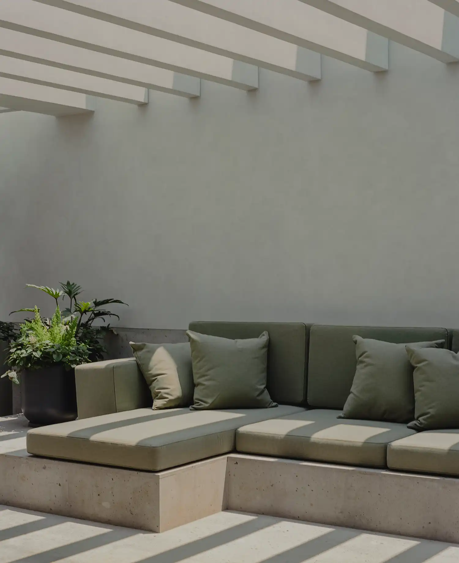 Minimalist outdoor terrace with olive green modular sofa under a white wooden pergola.