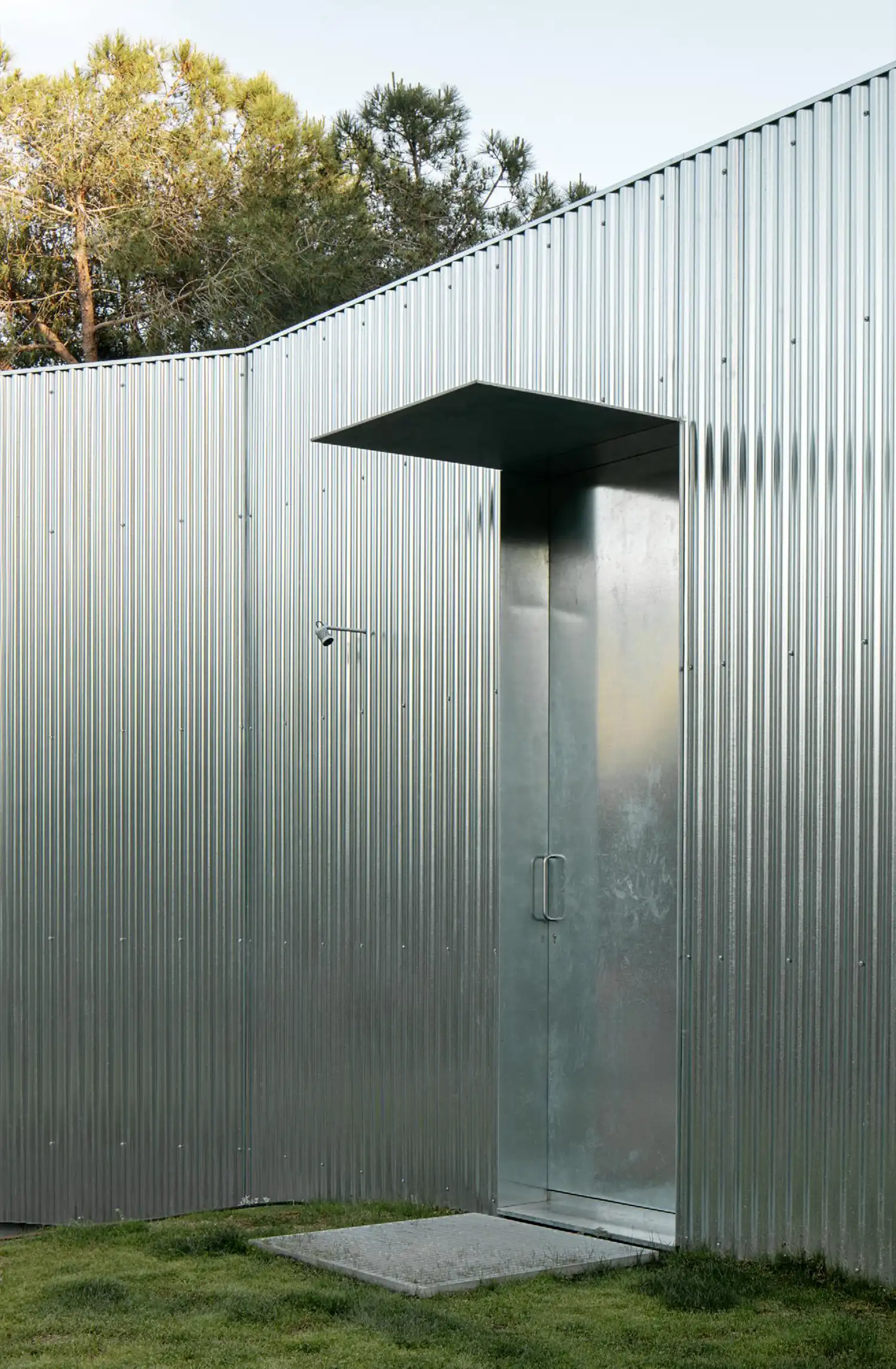 A minimalist entrance with a tall, flush-mounted steel door and a simple rectangular metal canopy.
