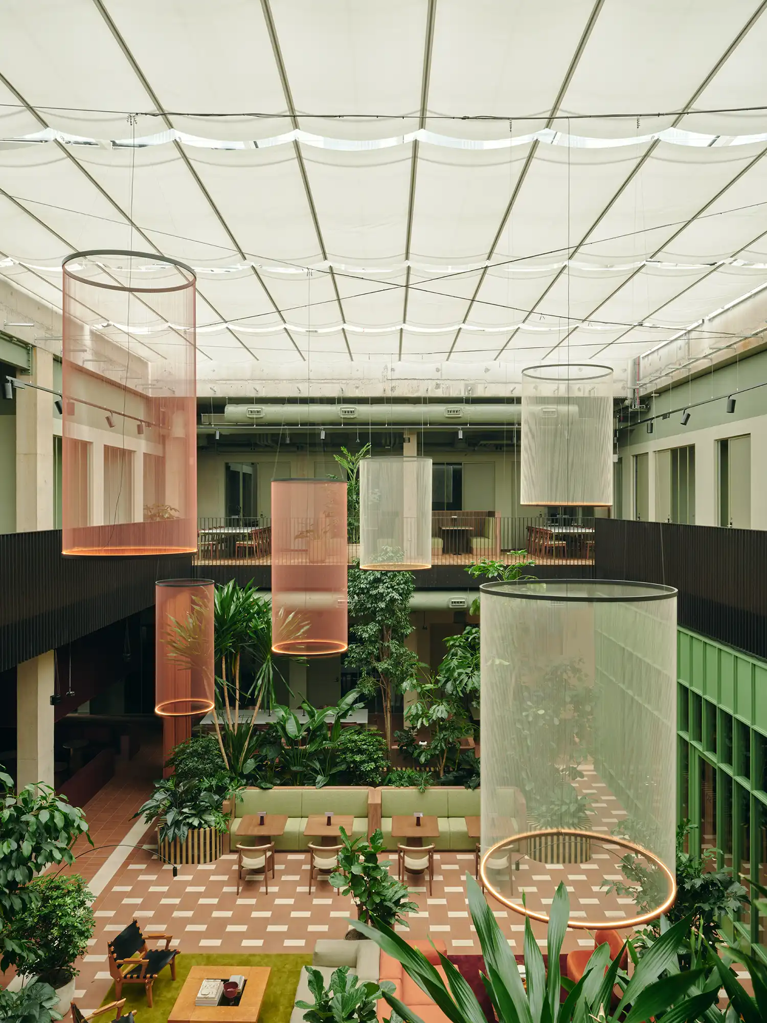 High-angle view of a double-height office atrium with cylindrical mesh pendants and lush planting.