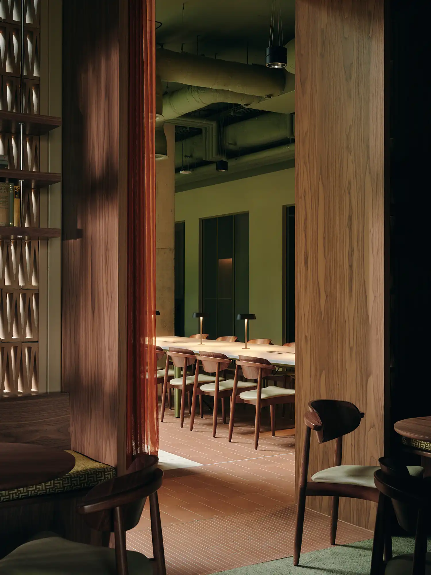 Long communal wooden work table with individual brass desk lamps in a moody interior.