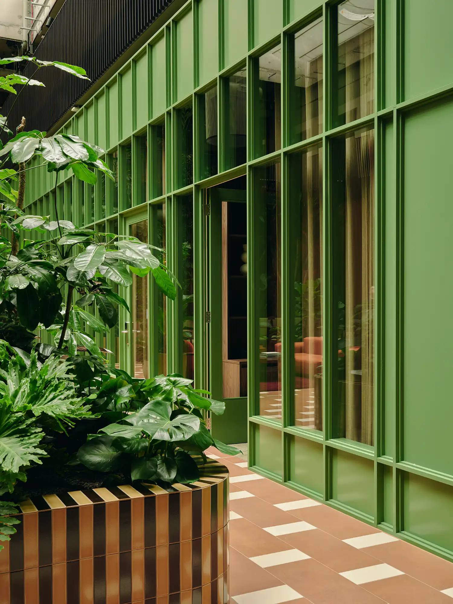 Exterior view of green-painted timber and glass meeting rooms adjacent to indoor planters.