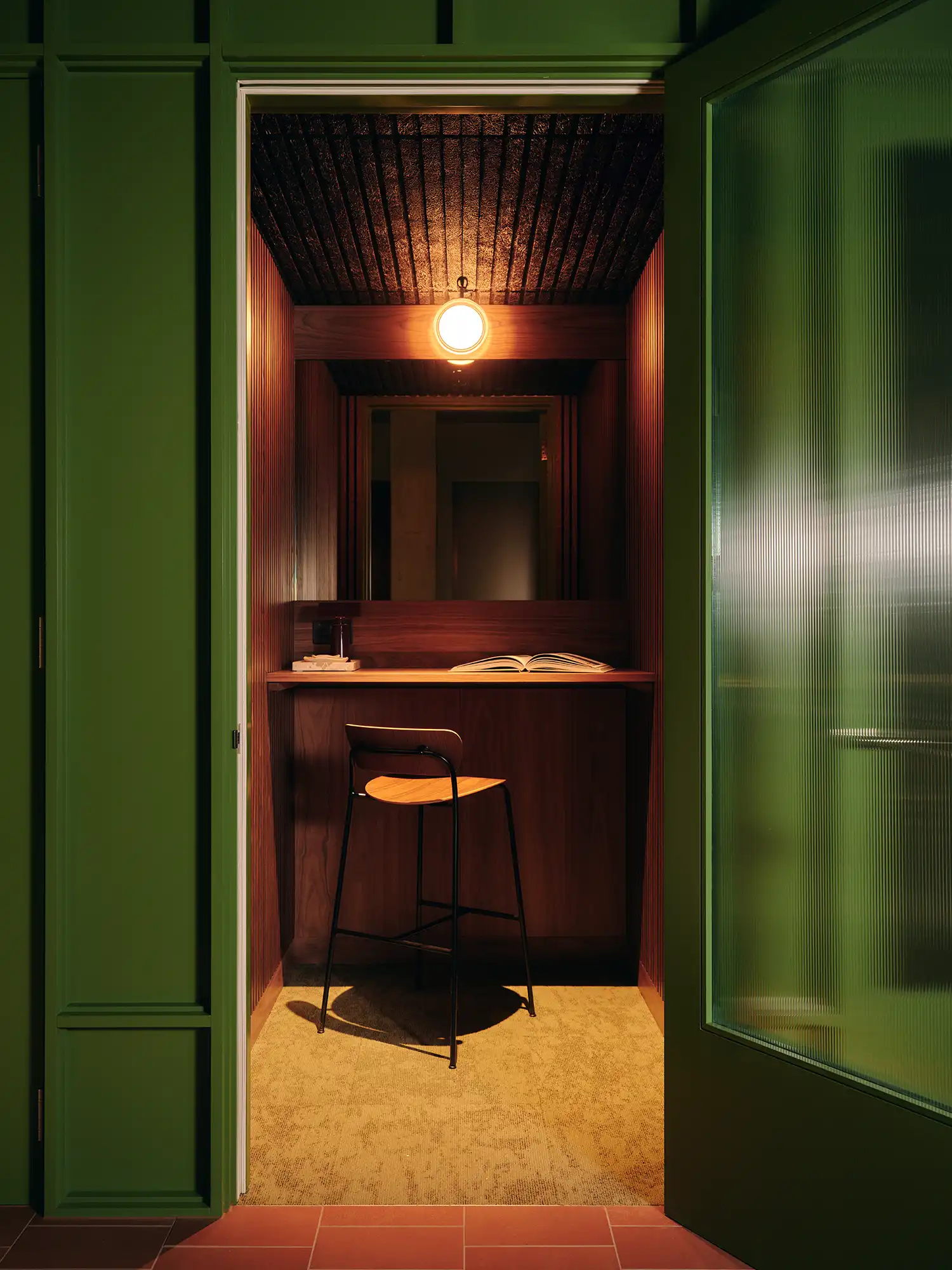 A private green phone booth or focus room with a warm wood desk and a single globe light.