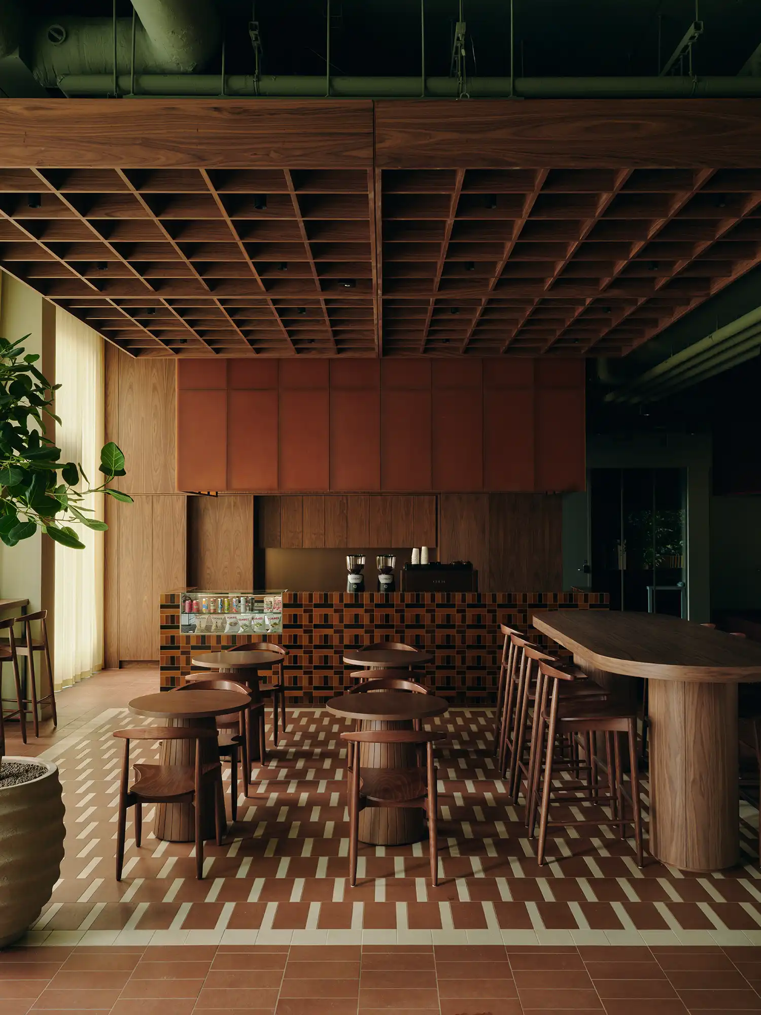 Café area with a grid-patterned tile counter, walnut cafe tables, and wood-slat ceiling.