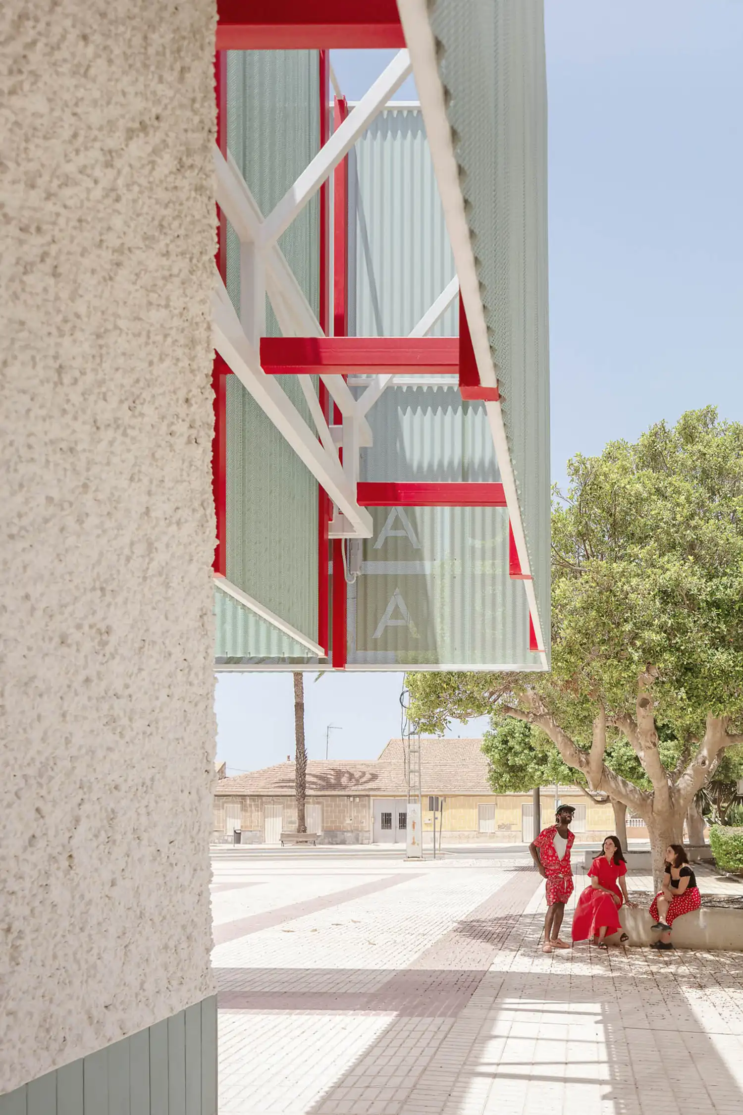 Detail of the red steel structure supporting the perforated metal facade at the Balsapintada Cultural Center.