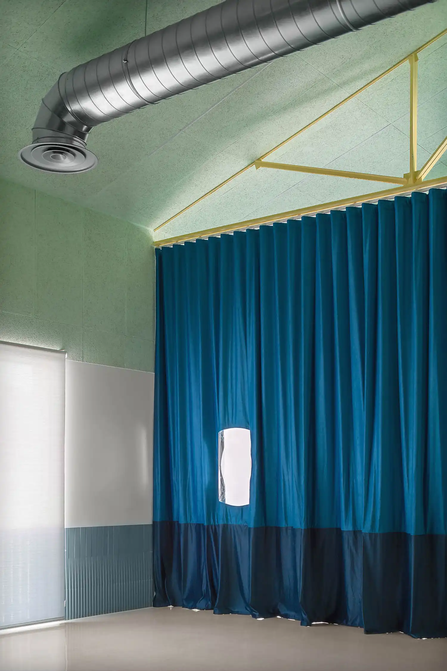 Interior of a multipurpose room featuring a high ceiling, exposed ventilation ducts, and a large teal curtain.