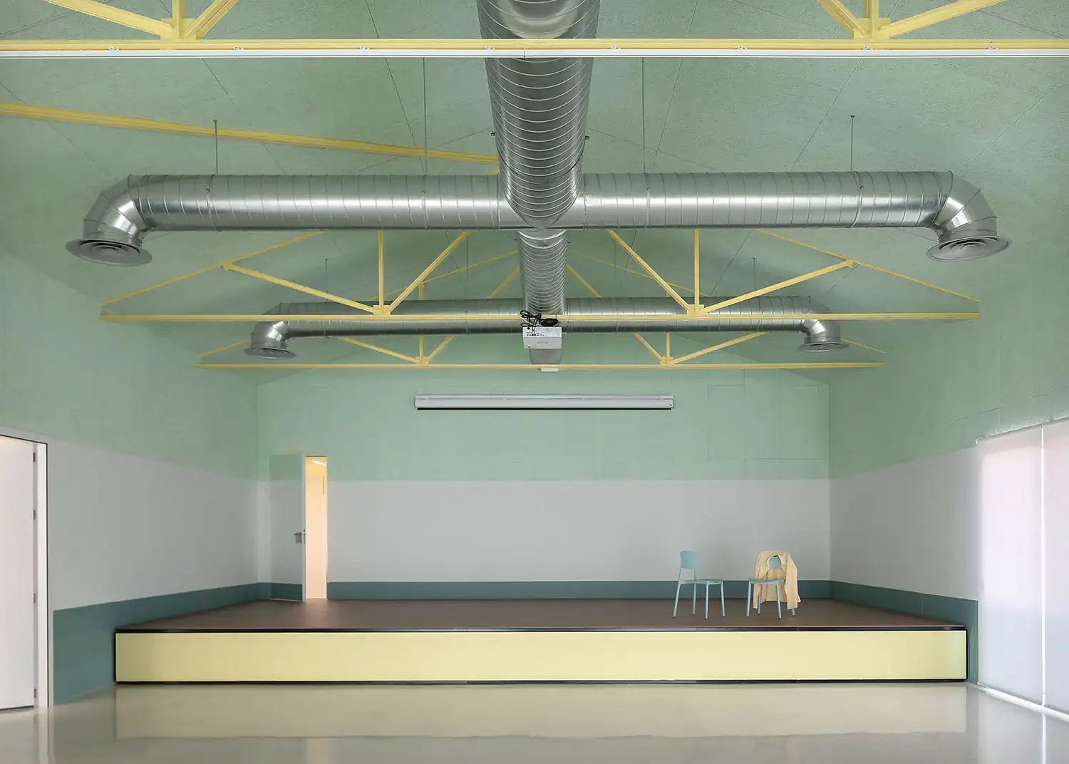 Wide view of the main hall stage with mint green walls and exposed industrial-style ventilation.