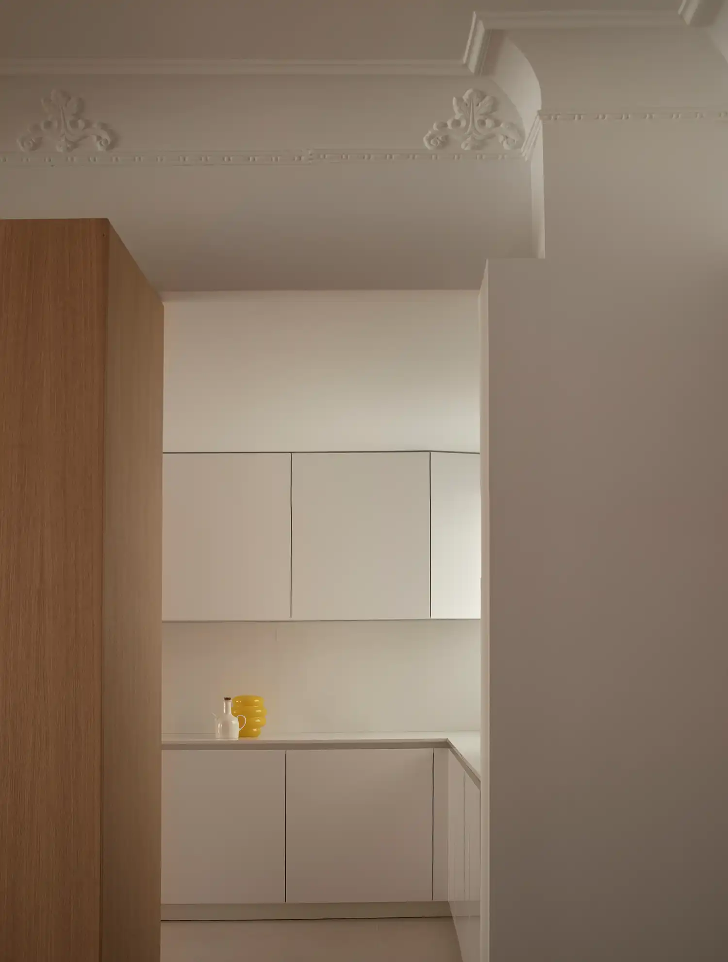 Minimalist white kitchen cabinetry viewed through a transition between white walls and oak.