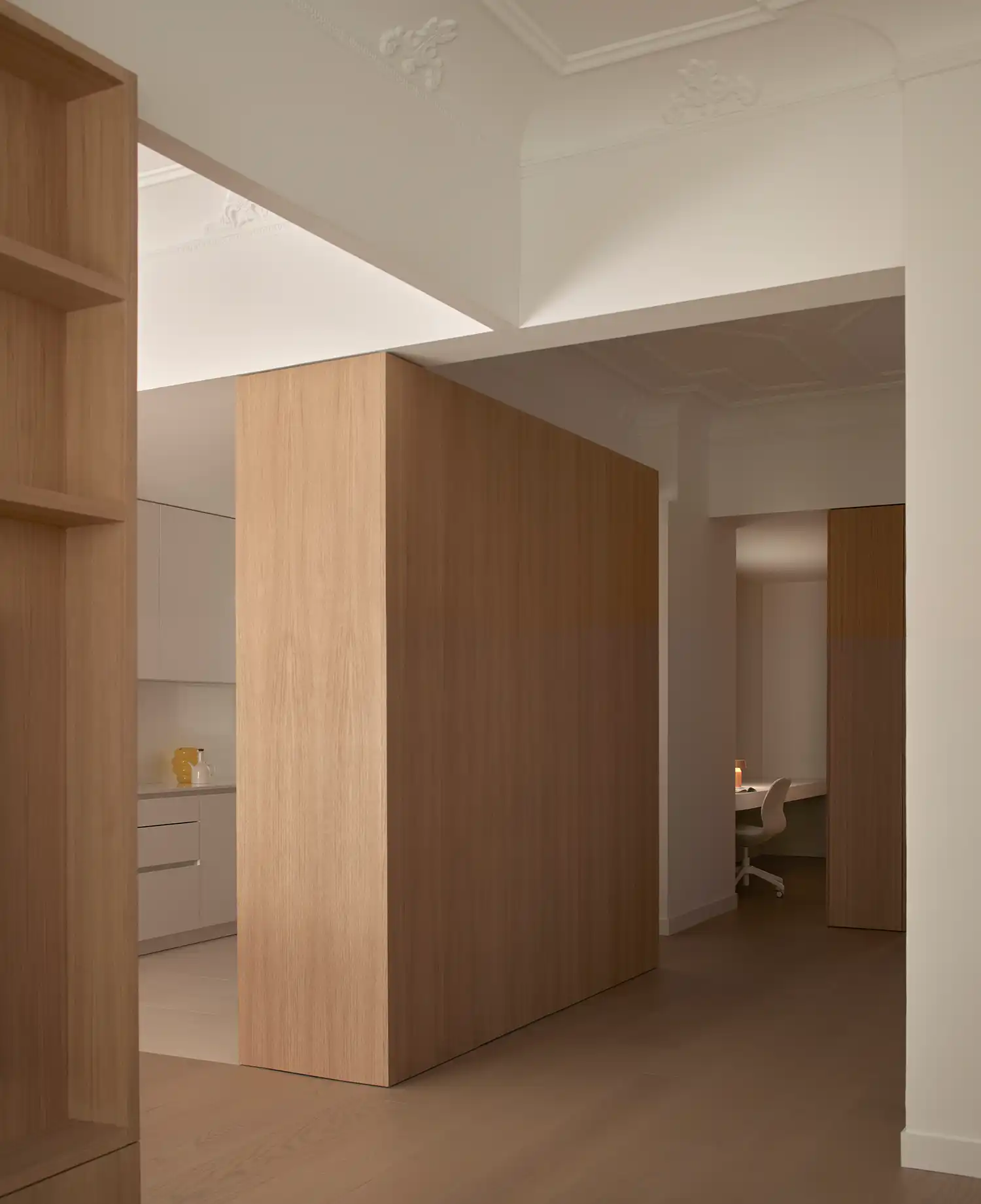 Perspective view through oak volumes toward a minimalist kitchen and study area.