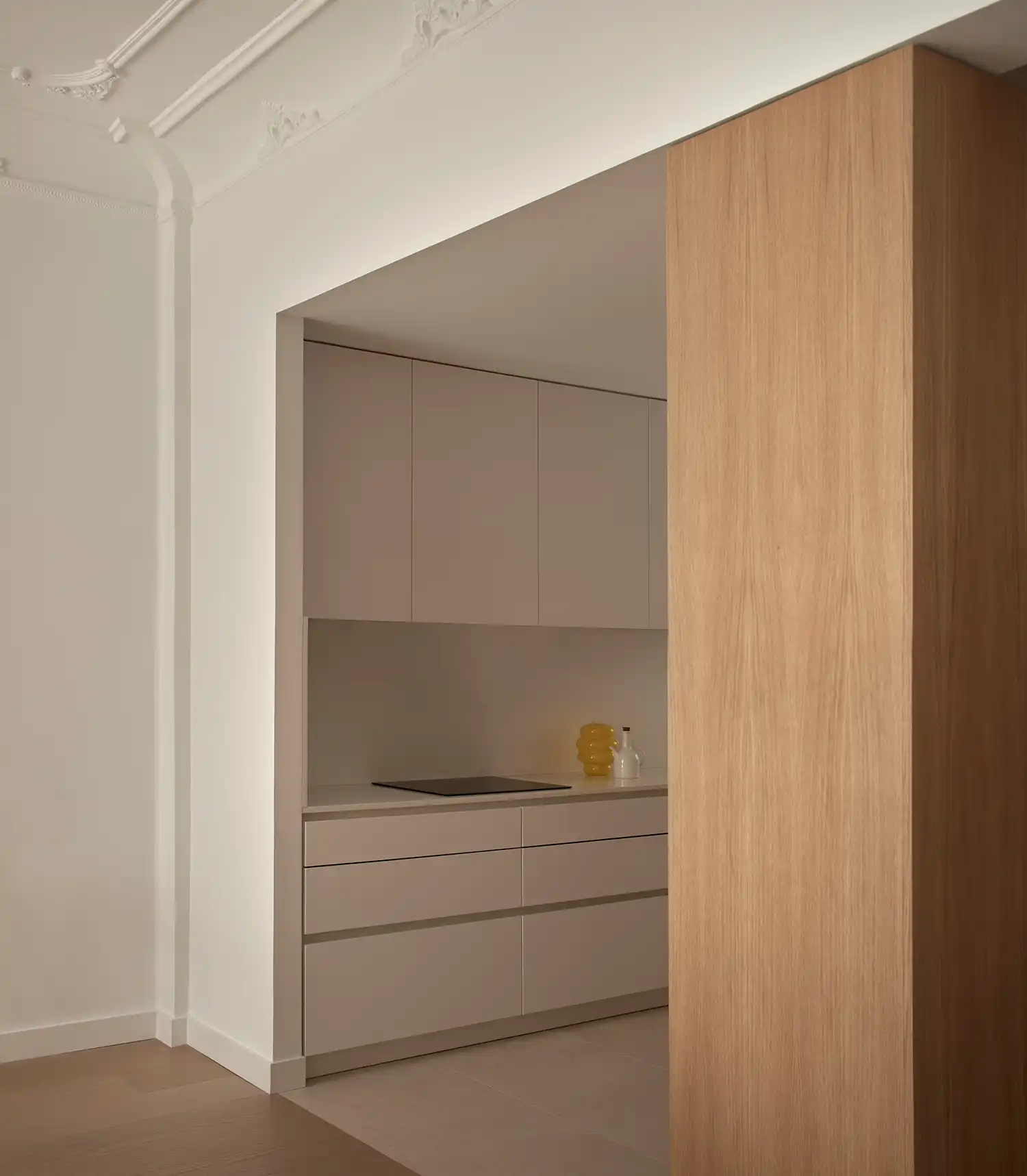 Corner view of a sleek white kitchen island next to a massive natural oak volume.