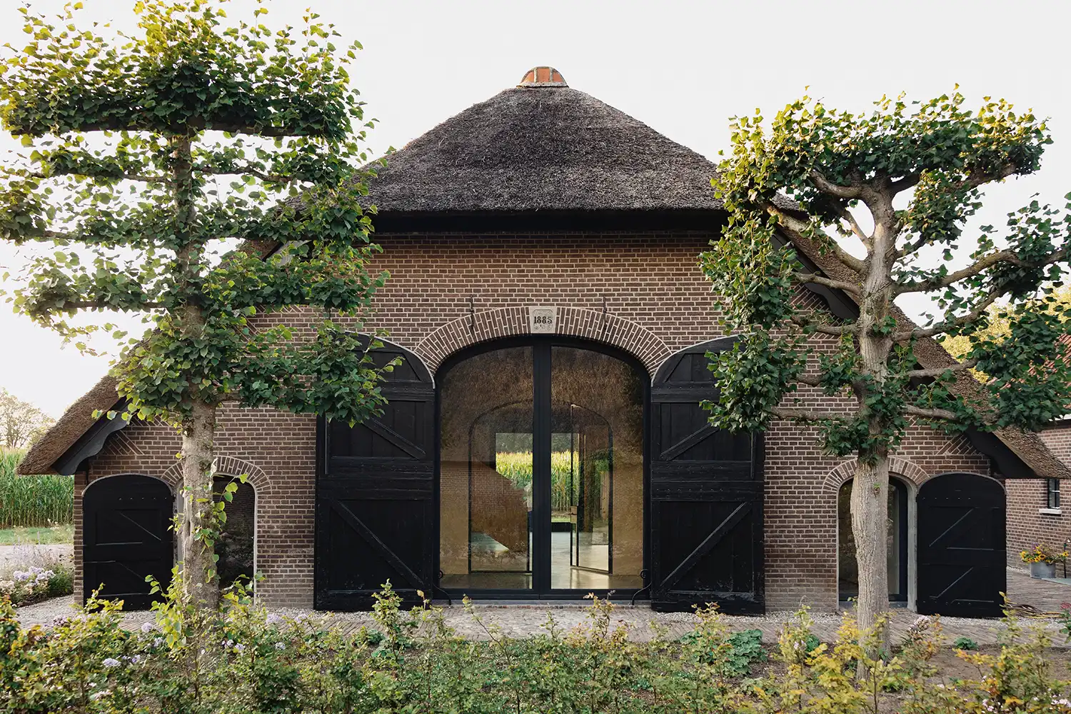 Large arched glass doors with black timber shutters on a brick barn facade.