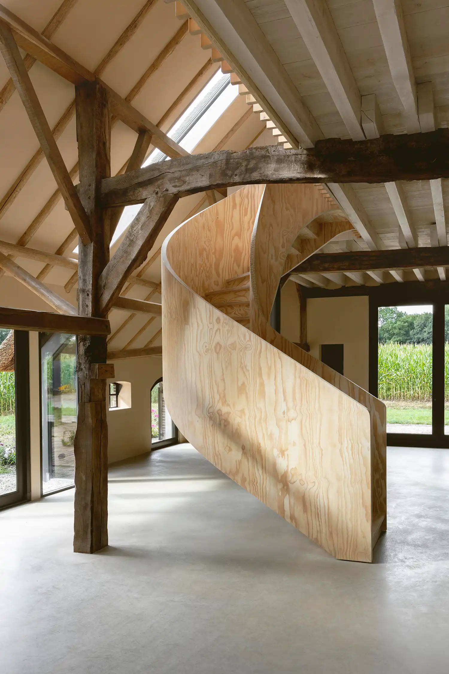 Self-supporting spiral staircase in pine plywood under a skylight in a barn.