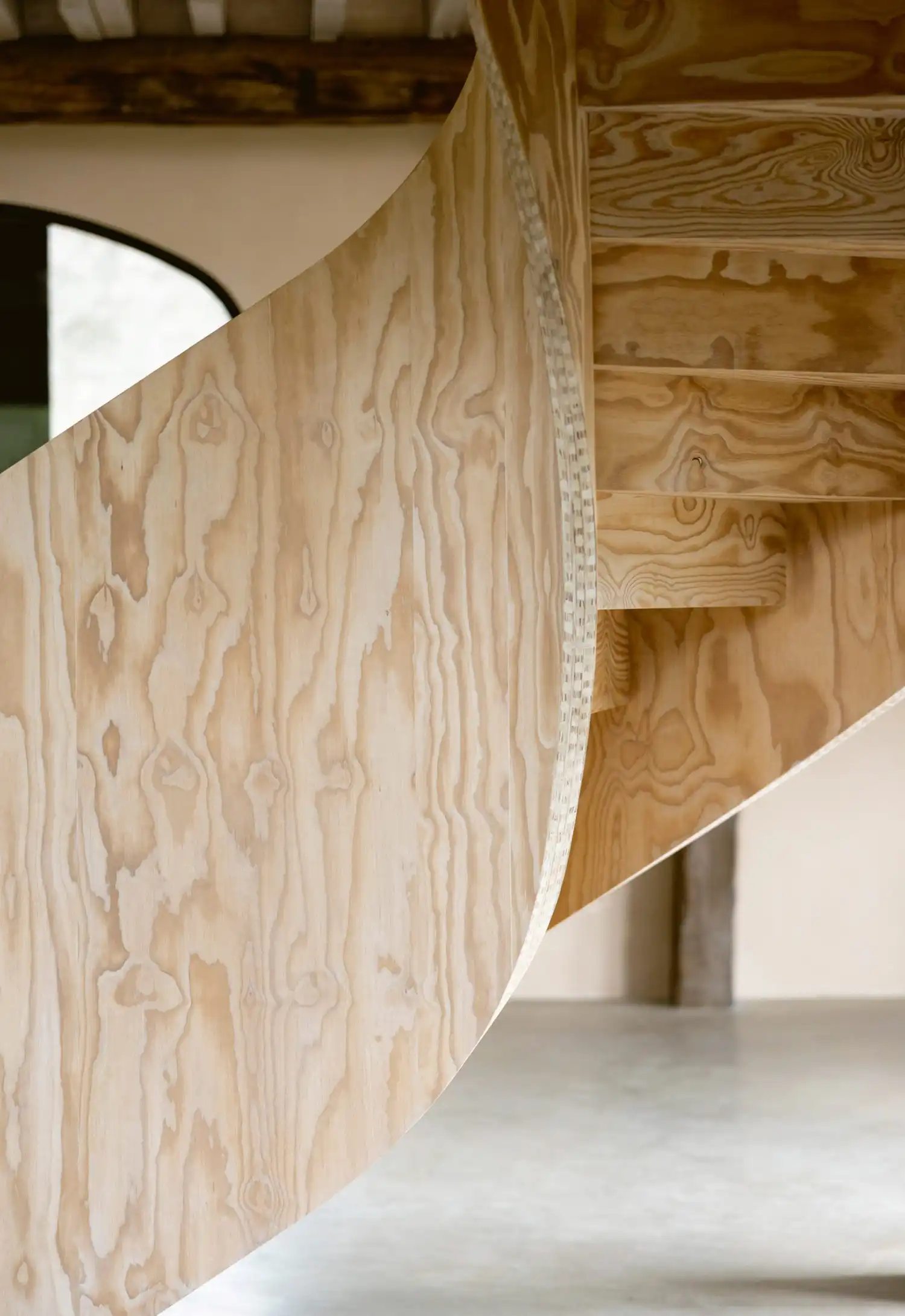 Close-up of pine plywood grain and precise joinery on a spiral staircase balustrade.
