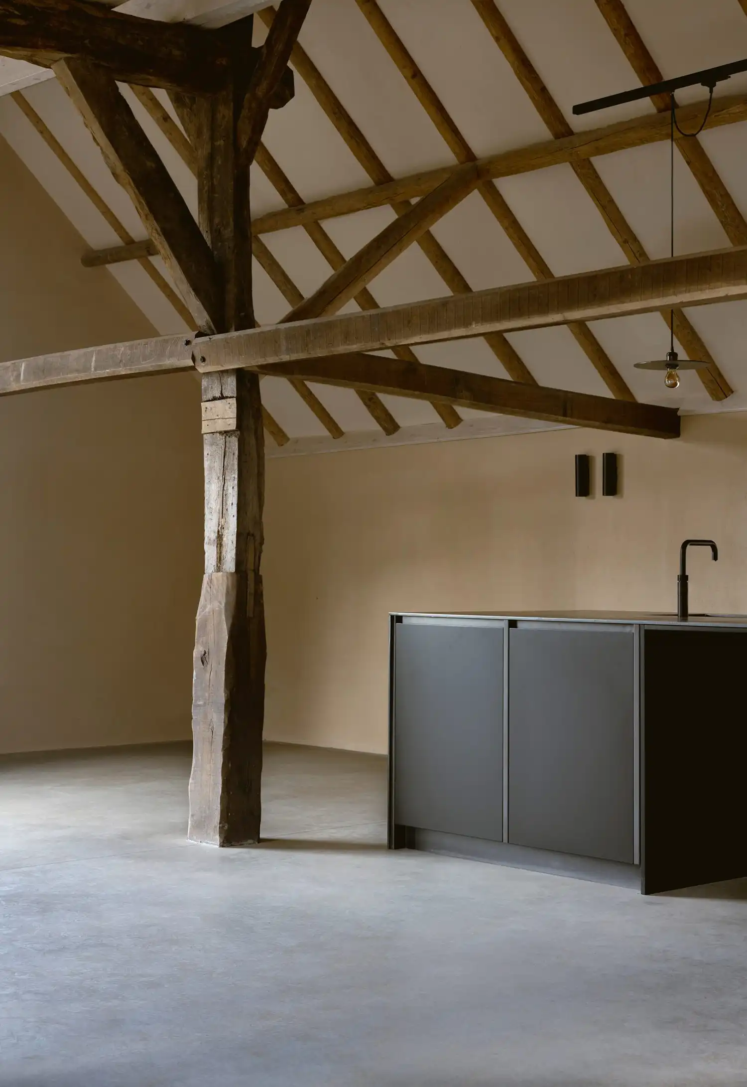 Minimalist black kitchen island set against lime plaster walls and an original timber post.