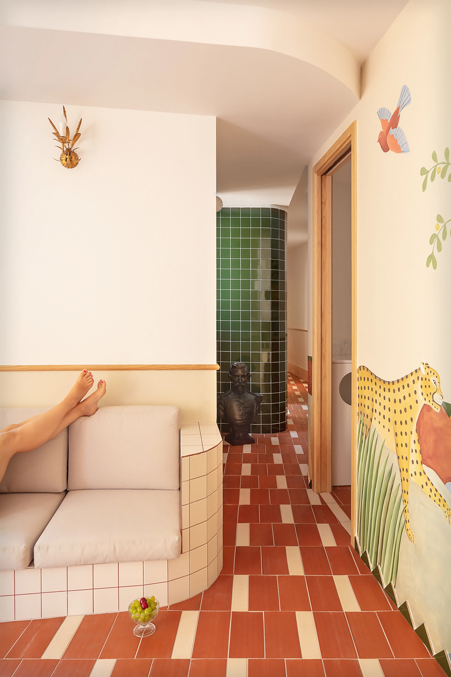A view from a tiled sofa toward a green tiled curved wall and a hallway with a jungle mural in El Desfile de la Puri.