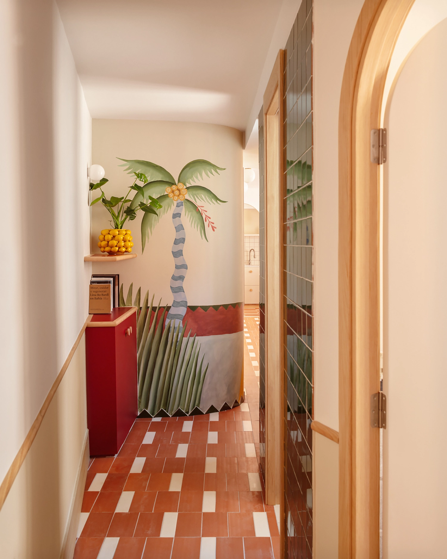 A narrow hallway in a Valencia apartment featuring a palm tree mural and a deep red storage cabinet.