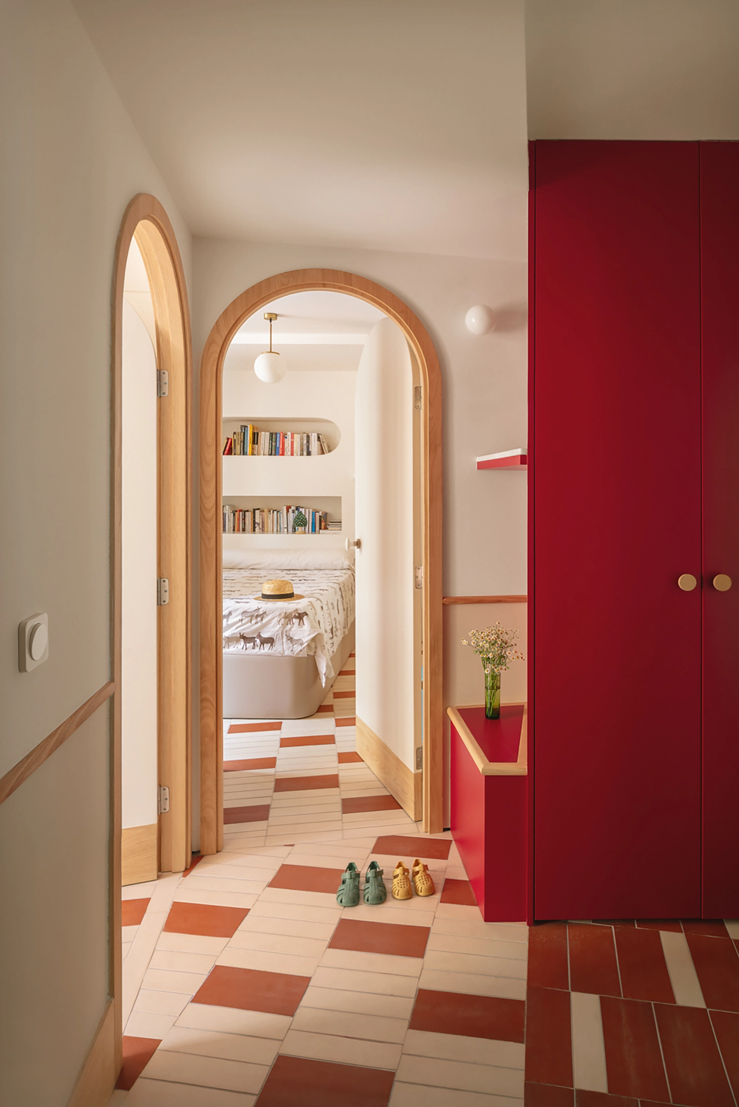 An arched doorway leading to a bedroom with built-in bookshelves and a large burgundy wardrobe in the foreground.