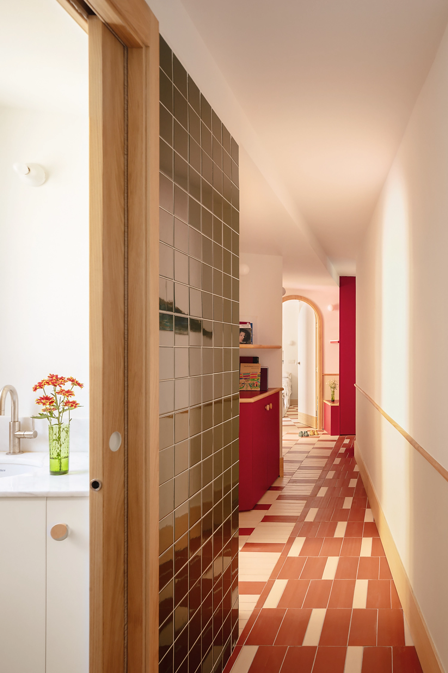 A long hallway view showing the rhythmic terracotta floor and a dark green tiled wall in a Valencia renovation.