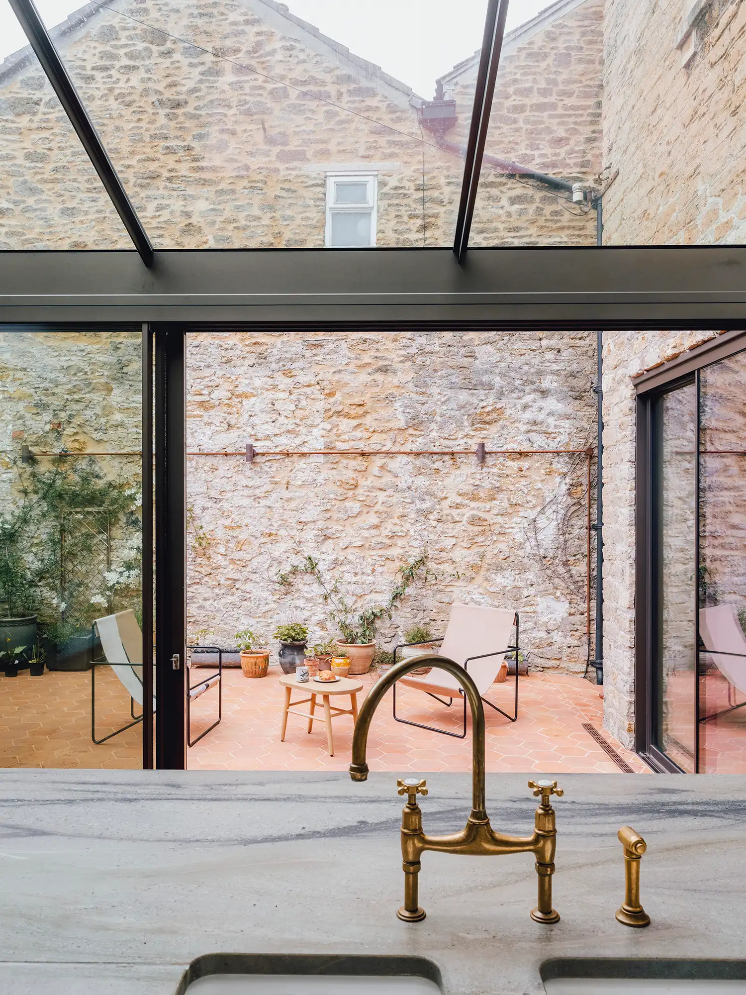 View from a kitchen sink through a large glass door into a stone-walled courtyard.